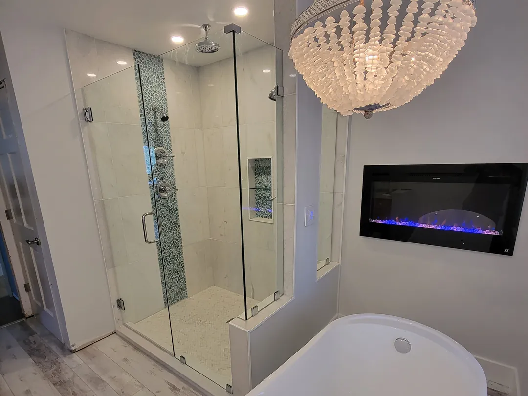 A frameless shower beside a freestanding tub under a beaded chandelier