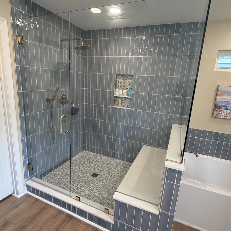 A frameless shower with gold hinges and pull, blue vertical tile and a bench