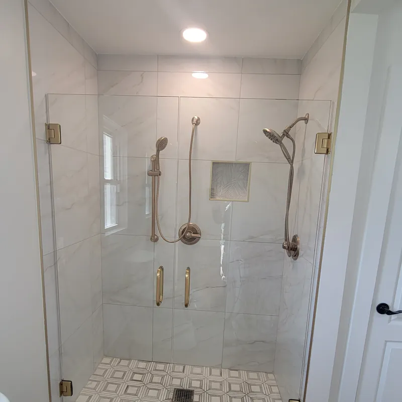 A frameless shower door with gold hinges and handles, white marble-look tile