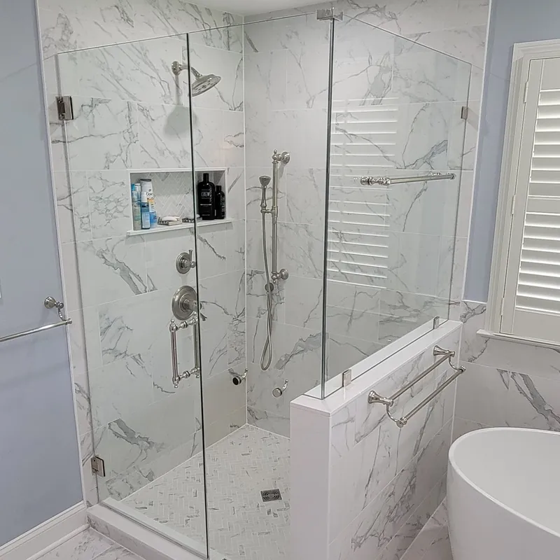 A frameless shower on a half wall with silver hinges and a silver towel bar