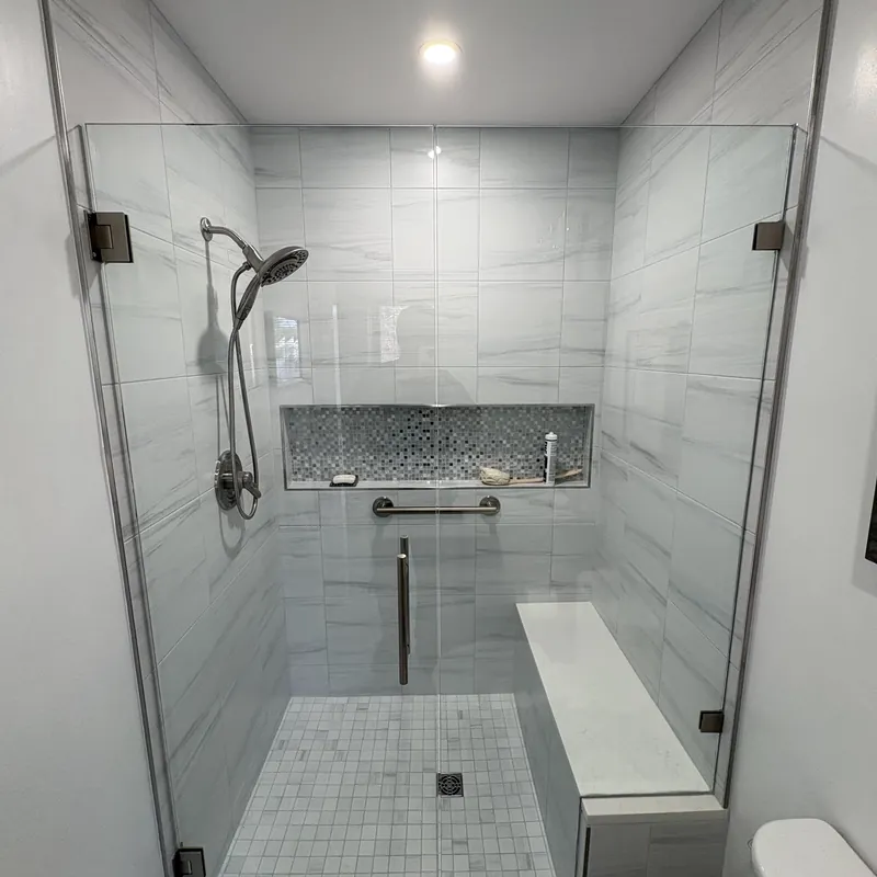 A frameless shower with silver hinges, a long tiled niche and a grab bar