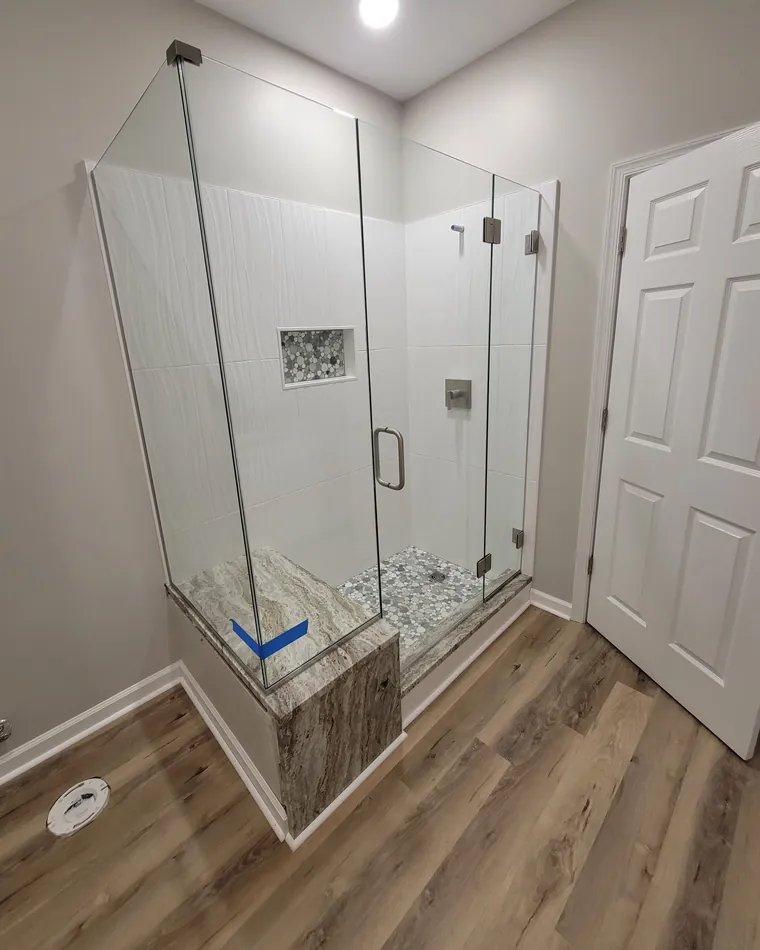 A frameless corner shower whose glass is built around a marble-topped bench
