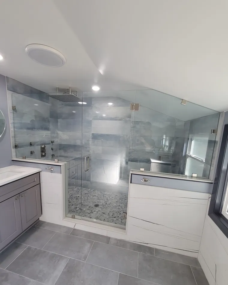 A large glass shower on two half walls, its top panels following a sloped ceiling