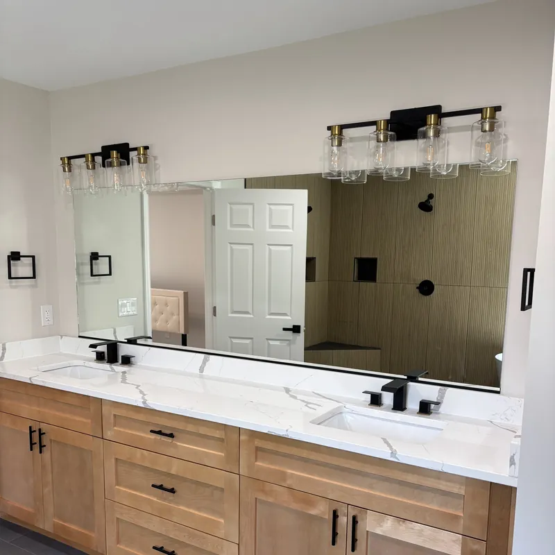 A wide mirror over a double vanity with black faucets and wood cabinets